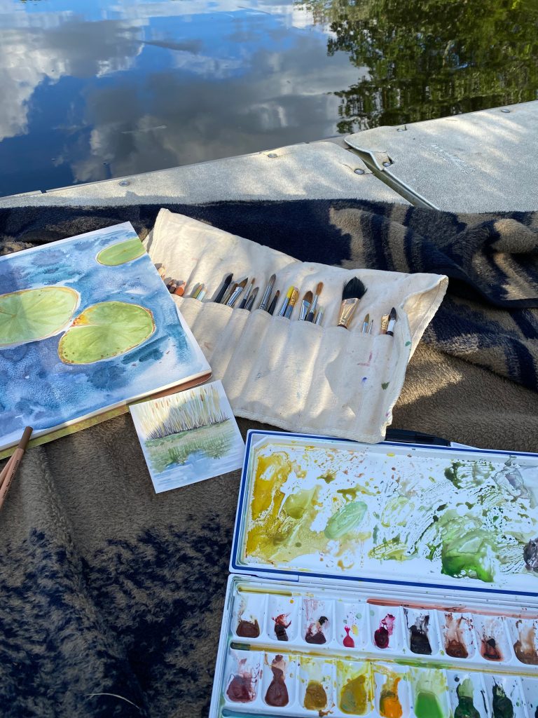 Rebekah Lowell's nature journaling materials by the water. Brushes, watercolors, and a journal.