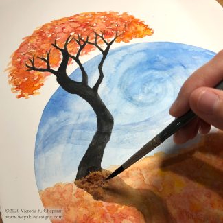 A black tree trunk is silhouetted against a blue sky with bright orange leaves and ground. A hand is actively painting this watercolor piece with a brush. Art by Victoria K. Chapman.