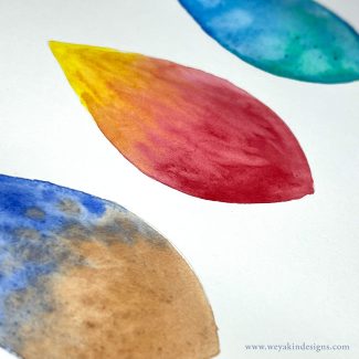 A close-up photo of tear-drop shaped watercolors in different colors across a page. www.weyakindesigns.com
