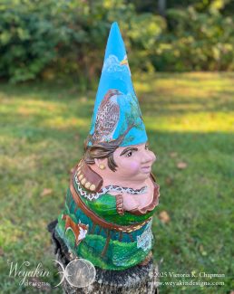 A garden gnome painted with a hawk, snake, fox, and other animals sits on top of a log in an outdoor background. Art by Victoria K. Chapman.